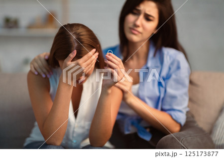 Divorce. Compassionate Young Woman Supporting Depressed Friend Showing Ring After Breakup Sitting On Sofa At Home. 125173877