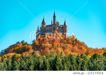 Hohenzollern castle on the hilltop, surrounded by autumn forest, under a blue sky 125173918