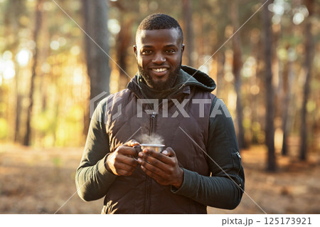 Positive african man drinking tea at forest, camping and hiking concept, empty space 125173921
