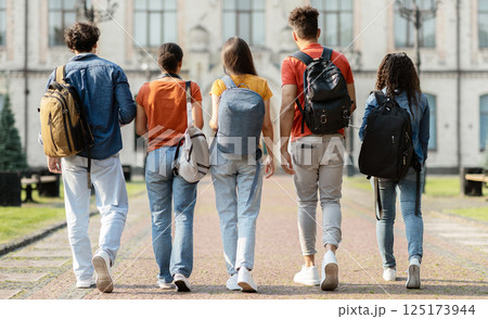 Group of five students with backpacks walking at university campus together, rear view of multiethnic young people going to classes, diverse college friends spending time outdoors after lessons 125173944