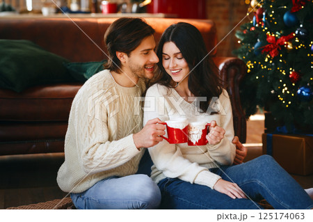 Couple in love having xmas cocoa next to Christmas tree at home, free space 125174063