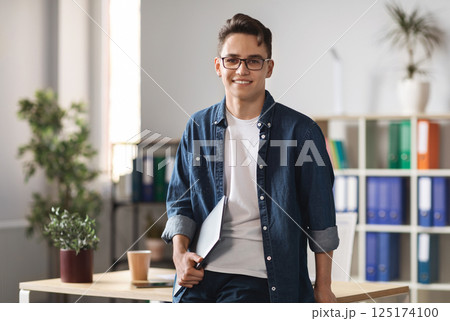 Portrait Of Handsome Young Male Entrepreneur Holding Laptop And Posing In Office Interior, Confident Millennial Man In Casual Clothes Standing Near Desk And Smiling At Camera, Copy Space Portrait Of Handsome Young Male Entrepreneur Holding Laptop And Posing In Office Interior, Confident Millennial Man In Casual Clothes Standing Near Desk And Smiling At Camera, Copy Space 125174100