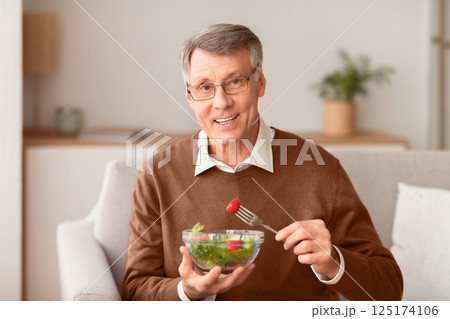 Healthy Nutrition. Senior Man Enjoying Vegetable Salad Smiling To Camera Sitting On Sofa At Home. Selective Focus Healthy Nutrition. Senior Man Enjoying Vegetable Salad Smiling To Camera Sitting On Sofa At Home. Selective Focus 125174106
