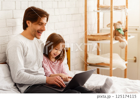 Preschool girl spending time with her daddy on weekend at home, using laptop in bedroom, copy space 125174115