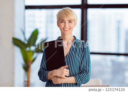 Middle-Aged Entrepreneur Lady Holding Folder Smiling At Camera Standing Near Window In Office. Business Career Concept Middle-Aged Entrepreneur Lady Holding Folder Smiling At Camera Standing Near Window In Office. Business Career Concept 125174120