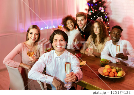 Happy New Year. Millennial Friends Holding Champagne Glasses Toasting Looking At Camera Sitting At Dinner Table At Home. 125174122