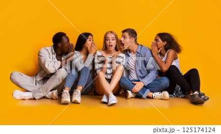 Shocked girl listening to her international classmates whispers, yellow background, panorama Shocked girl listening to her international classmates whispers, yellow background, panorama 125174124