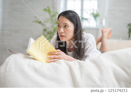 ベッドで読書をするきれいな女性｜勉強｜趣味｜健康的な暮らしイメージ｜ウェルビー女子｜ウェルビーイング 125174251