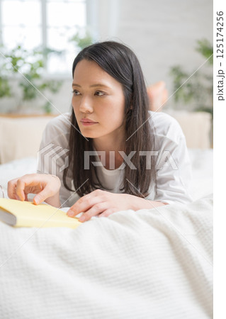 ベッドで読書をするきれいな女性｜勉強｜趣味｜健康的な暮らしイメージ｜ウェルビー女子｜ウェルビーイング 125174256