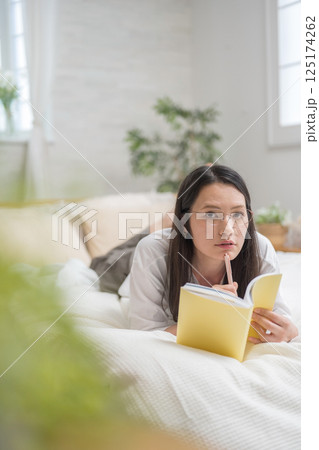 ベッドで読書をするきれいな女性｜勉強｜趣味｜健康的な暮らしイメージ｜ウェルビー女子｜ウェルビーイング 125174262