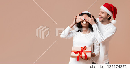 Romantic Boyfriend Covering Eyes of His Afro Girlfriend And Giving New Year Or Christmas Present, Making Surprise. Yellow Background With Free Space 125174272