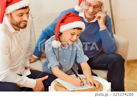Christmas. Boy With Father And Grandpa Writing Letter To Santa Claus Sitting Together On Couch At Home. Selective Focus Christmas. Boy With Father And Grandpa Writing Letter To Santa Claus Sitting Together On Couch At Home. Selective Focus 125174280