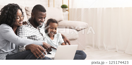 Joyful african american family of three using laptop at home together, watching movie or browsing internet 125174423