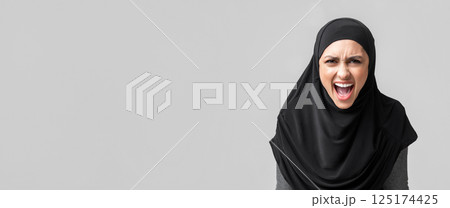 Angry muslim woman in hijab screaming loud, emotionally protesting about something over gray background with free space 125174425