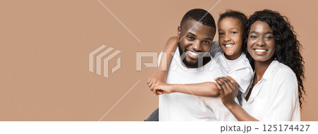 Portrait of positive black family of three, mother, father and their little daughter looking at camera over yellow background, copy space 125174427