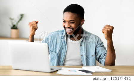 Great news. Euphoric african american entrepreneur celebrating business success with raised arms, looking at laptop screen with excitement Great news. Euphoric african american entrepreneur celebrating business success with raised arms, looking at laptop screen with excitement 125174456