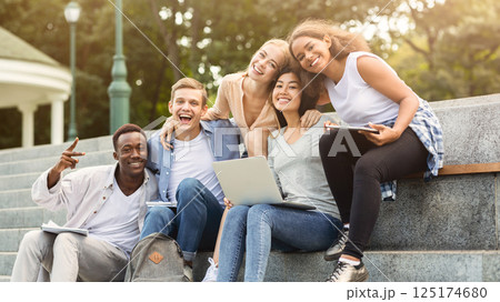 Happy friends international students posing while studying with laptop in city, sitting on stairs, empty space Happy friends international students posing while studying with laptop in city, sitting on stairs, empty space 125174680