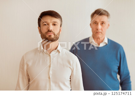 Serious Middle Aged Son And His Elderly Father Standing Looking At Camera On White Background. Selective Focus 125174711