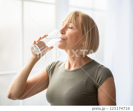 Fit senior woman drinking clear water during her workout break at home. Mature Caucasian lady staying hydrated after sports training. Healthy lifestyle and wellness concept Fit senior woman drinking clear water during her workout break at home. Mature Caucasian lady staying hydrated after sports training. Healthy lifestyle and wellness concept 125174719