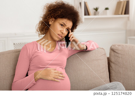 Sad afro pregnant woman talking on phone, having serious conversation with doctor 125174820