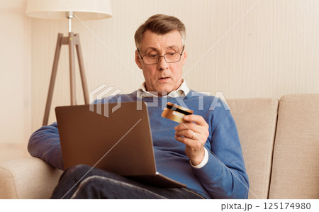 Online Shopping. Senior Man Using Credit Card And Laptop Computer Sitting On Sofa At Home. Selective Focus 125174980