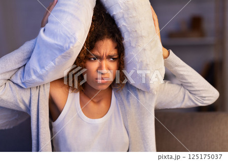 Annoyed woman covering ears with pillow, suffering from noisy neighbours Annoyed woman covering ears with pillow, suffering from noisy neighbours 125175037