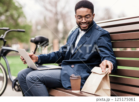 Time for snack. Businessman having lunch with his bicycle nearby, sitting in park Time for snack. Businessman having lunch with his bicycle nearby, sitting in park 125175061