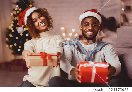 Happy New Year. Afro couple stretching gift boxes and smiling in front of Christmas tree Happy New Year. Afro couple stretching gift boxes and smiling in front of Christmas tree 125175088