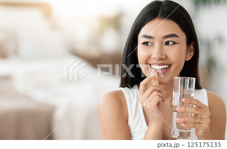Diet, nutrition, healthy eating concept. Close Up Of Happy Smiling Asian Woman Taking Supplement Pill And Holding Glass Of Fresh Water In Morning, copy space 125175135