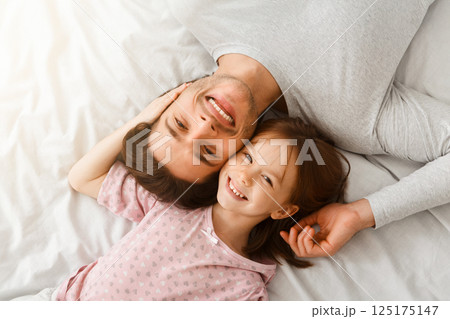 Top view of handsome young father and his cute little daughter looking at camera and smiling, lying on bed at home, just woke up, affectionate concept 125175147
