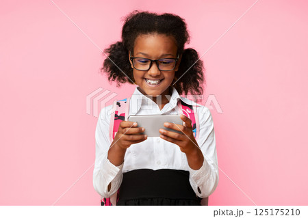 Gadgets In School. Girl Using Smartphone Playing Mobile Game During Break Standing Over Yellow Studio Background. Gadgets In School. Girl Using Smartphone Playing Mobile Game During Break Standing Over Yellow Studio Background. 125175210