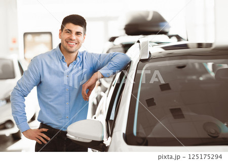 Ownership Concept. Handsome man leaning on his brand new car standing in dealership center, free space 125175294