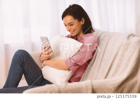 Domestic Rest. Smiling girl enjoying web surfing on smartphone at home, reading love message from boyfriend, free space Domestic Rest. Smiling girl enjoying web surfing on smartphone at home, reading love message from boyfriend, free space 125175339