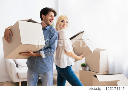Flat Ownership. Cheerful Spouses Holding Moving Boxes Standing Back-To-Back In New Home. Copy Space 125175345