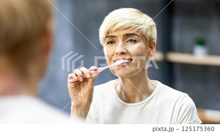 Toothcare. Middle-Aged Lady Brushing Perfect Teeth Using Toothbrush Standing In Bathroom Indoor. Selective Focus 125175360
