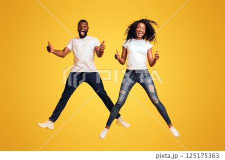 Happy Black Man And Woman Are Jumping In The Air And Showing Thumbs Up, yellow background Happy Black Man And Woman Are Jumping In The Air And Showing Thumbs Up, yellow background 125175363