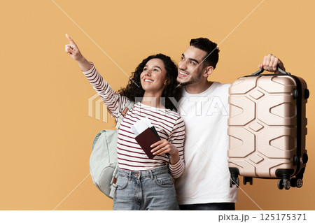 Travel Advertisement. Joyful Arab Couple With Suitcase And Passports Pointing Away At Copy Space On Yellow Background, Happy Middle Eastern Travellers Demonstrating Free Place For Ad, Panorama Travel Advertisement. Joyful Arab Couple With Suitcase And Passports Pointing Away At Copy Space On Yellow Background, Happy Middle Eastern Travellers Demonstrating Free Place For Ad, Panorama 125175371