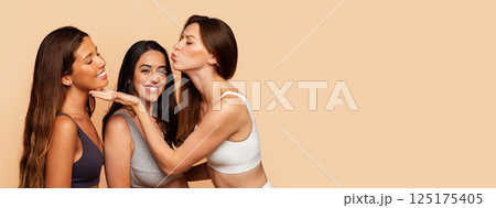 Three multiracial millennial women in underwear make air kissing, smiling, have fun, enjoy beauty care procedures on beige background. Health care and friendship, support, copy space Three multiracial millennial women in underwear make air kissing, smiling, have fun, enjoy beauty care procedures on beige background. Health care and friendship, support, copy space 125175405