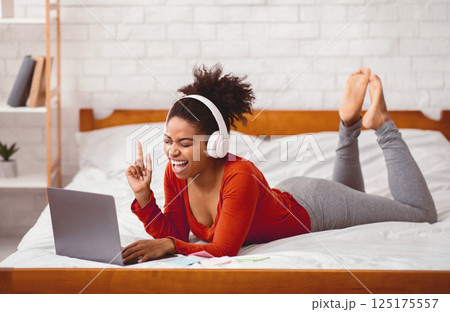 Weekend Leisure. Afro Woman In Headphones Using Laptop Listening To Music Relaxing On Bed At Home. Selective Focus 125175557