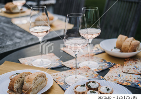 Glasses of rose wine and savory tarts arranged on an outdoor table set with decorative napkins and fresh bread. Al fresco dining, artisanal food, celebration gathering, slow living 125175598