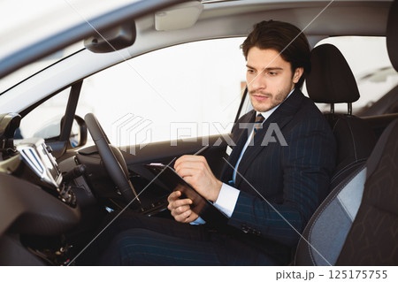 Serious Car Seller Sitting In Auto Taking Notes Checking Vehicle Before Selling In Dealership Center. Selective Focus Serious Car Seller Sitting In Auto Taking Notes Checking Vehicle Before Selling In Dealership Center. Selective Focus 125175755
