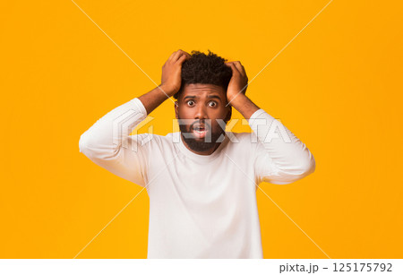 It's impossible. Shocked afro guy with open mouth touching his head over orange background It's impossible. Shocked afro guy with open mouth touching his head over orange background 125175792