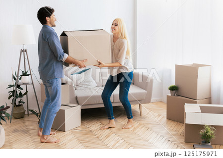 A couple moves a large cardboard box in a new apartment with bare feet and smiles. A couple moves a large cardboard box in a new apartment with bare feet and smiles. 125175971