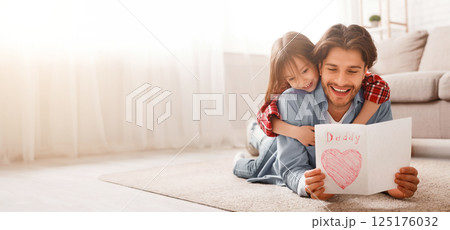 Happy father reading greeting self-made card while bonding with daughter on floor at home, free space 125176032