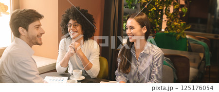Cheerful multiethnic business partners discussing strategy of new start up project in restaurant, having lunch, copy space Cheerful multiethnic business partners discussing strategy of new start up project in restaurant, having lunch, copy space 125176054