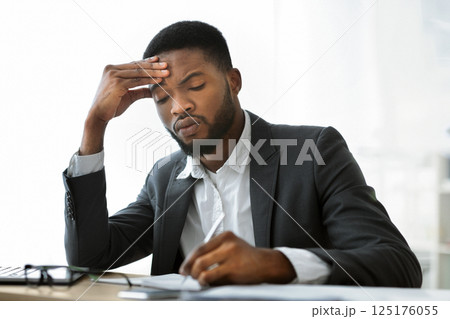 Busy afro businessman filling paperwork at workplace in modern office, free space Busy afro businessman filling paperwork at workplace in modern office, free space 125176055