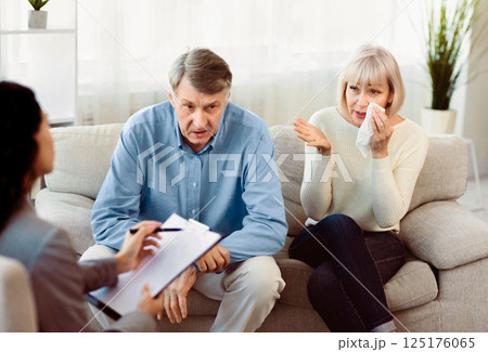 Marriage Counseling. Senior couple sitting on couch and talking to psychologist, doctor making notes, woman crying 125176065