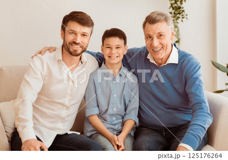 Smiling Boy With Father And Grandfather Sitting On Sofa Hugging And Looking At Camera At Home. Male Generation Family Portrait. Smiling Boy With Father And Grandfather Sitting On Sofa Hugging And Looking At Camera At Home. Male Generation Family Portrait. 125176264