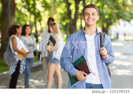 Attractive young guy student spending time with friends together after university, public park Attractive young guy student spending time with friends together after university, public park 125176335