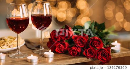 Romantic Dinner. Bouquet of flowers lying on the table, selective focus on bunch of roses, two glasses of red wine and candles on the wooden desk. Date concept, blurred background, banner, copy space 125176369
